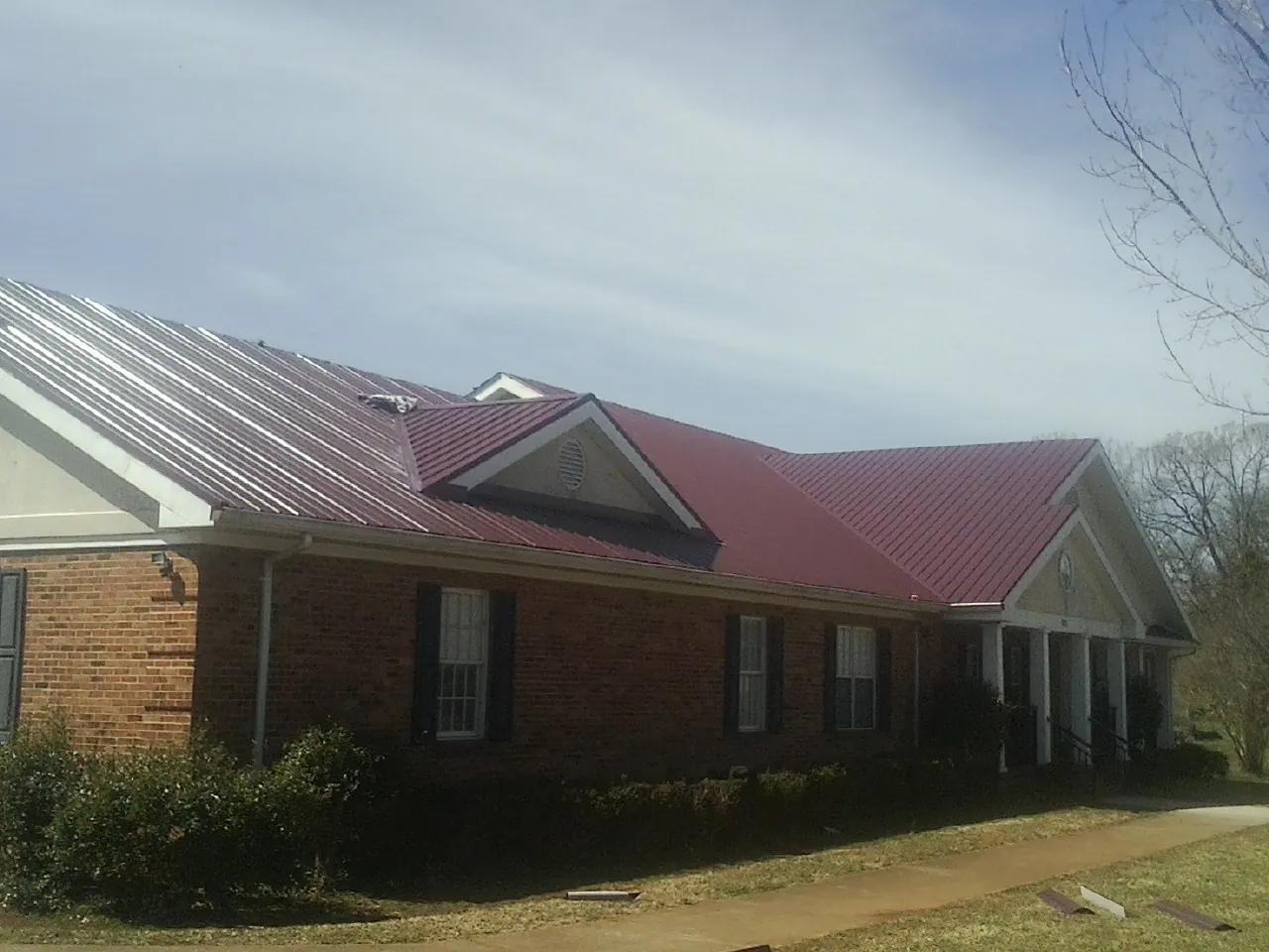 Red metal roof with gabled entries on a long brick building, from a Hail Damage Roof Repair job in Weogufka