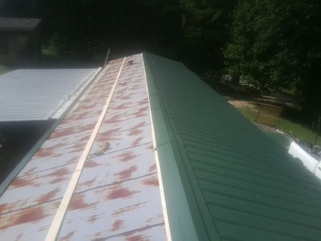 Old rusted panels beside newly installed green metal roofing — Wind Damage Roof Repair by Roofing Brothers in Weogufka