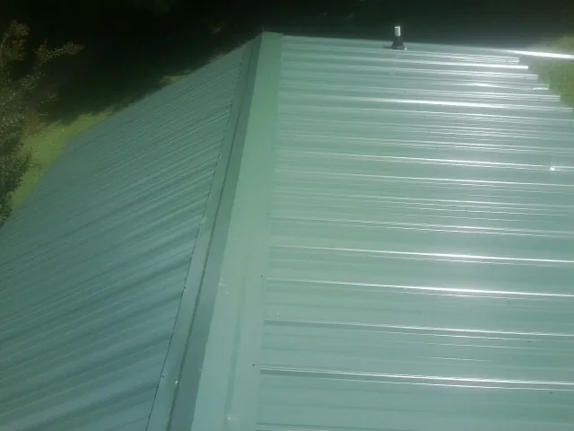 New green metal panels meeting at the ridge of a roof — Flat Roof Repair work by our crew in Weogufka