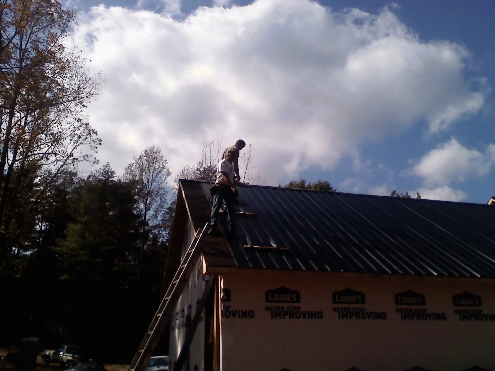 Roofer fastening dark metal panels high against a cloudy sky, from a Roof Inspection job in Weogufka