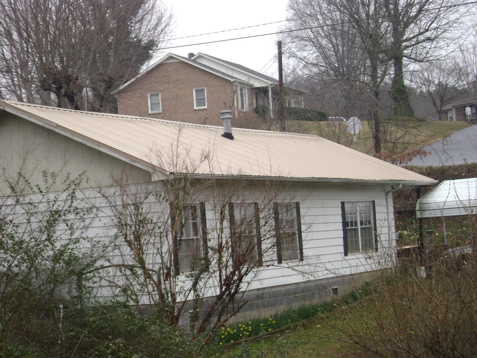 Tan metal roof on a white sided house set into a hillside — Commercial Roofing by Roofing Brothers in Weogufka