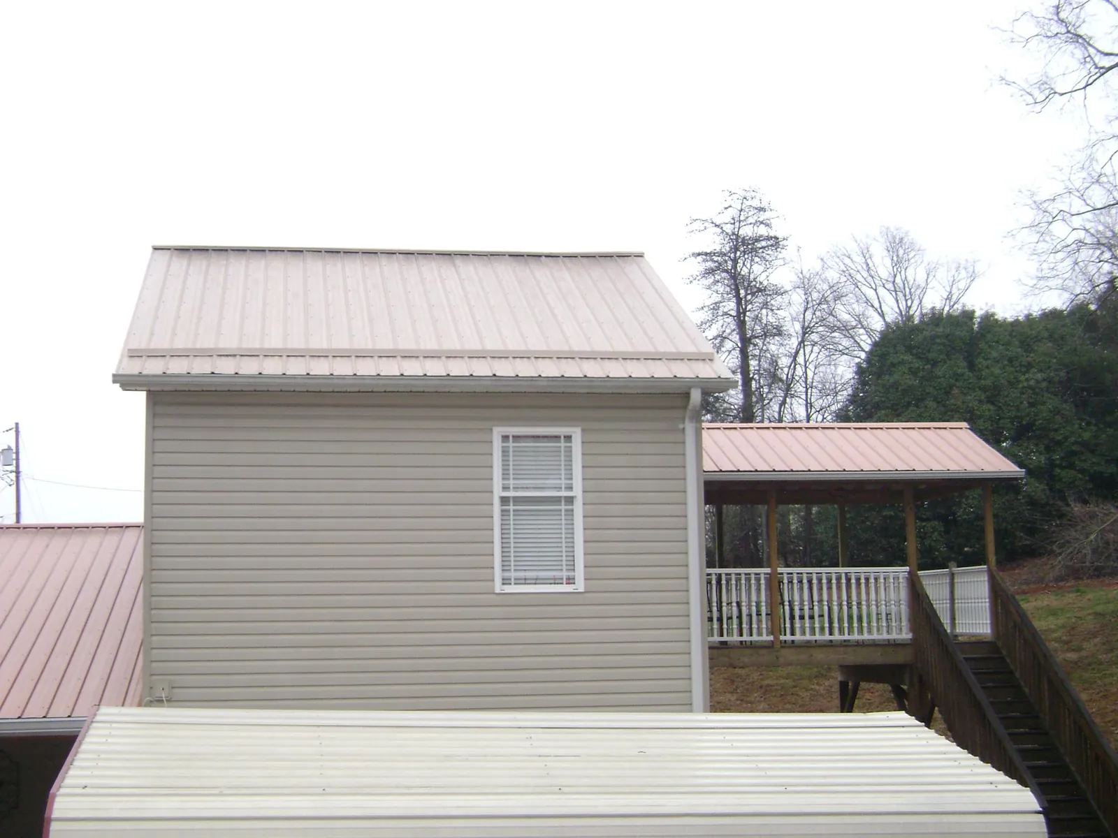 Tan metal roofs on a two story addition and attached porch, from a Roof Replacement job in Weogufka